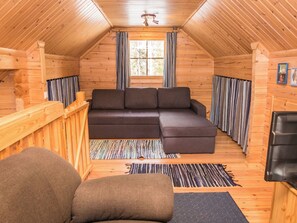 A cozy wooden cabin interior with a sectional sofa, a small table, and a fireplace.