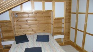 A wooden cabin room with a bunk bed, two pillows, and a patterned bedspread.