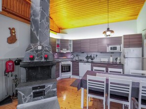 Eine moderne Küche mit Kamin aus Stein, Holzbalkendecke und integrierten Geräten.