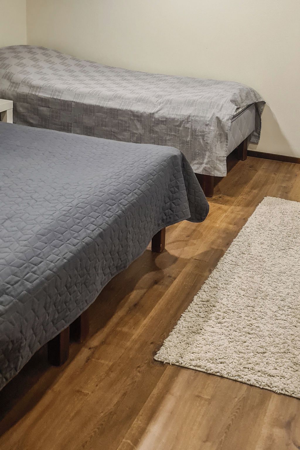A room with two beds, a wooden floor, and a white rug.