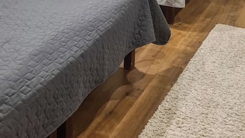 A room with two beds, a wooden floor, and a white rug.