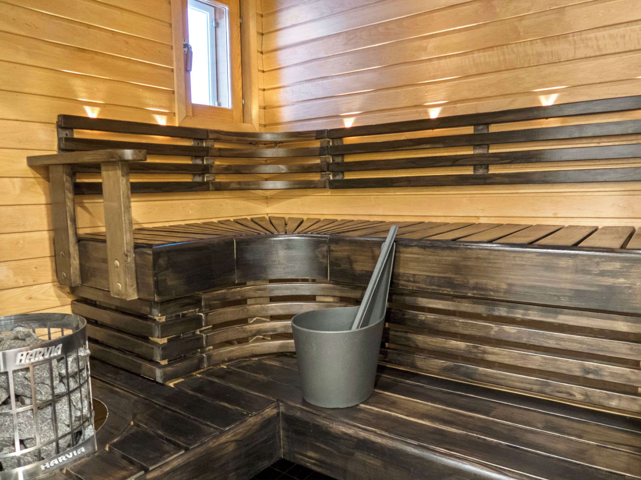 A sauna with wooden benches, a metal bucket, and a window.