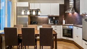 Et moderne køkken med hvide skabe, et rustfrit stål emfang og et spiseområde med et træbord og stole.
