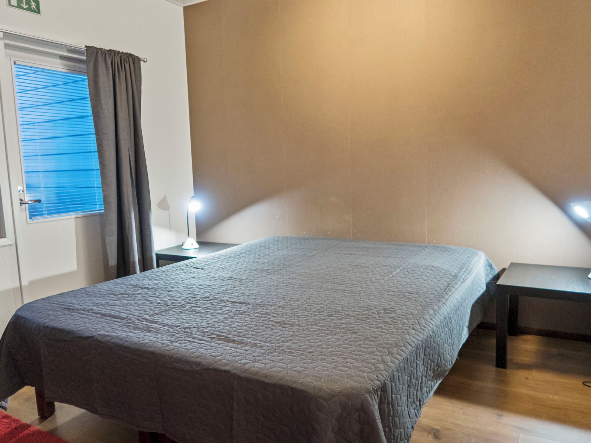 Een hotelkamer met een bed, nachtkastjes, een raam met gordijnen en een wandlamp.