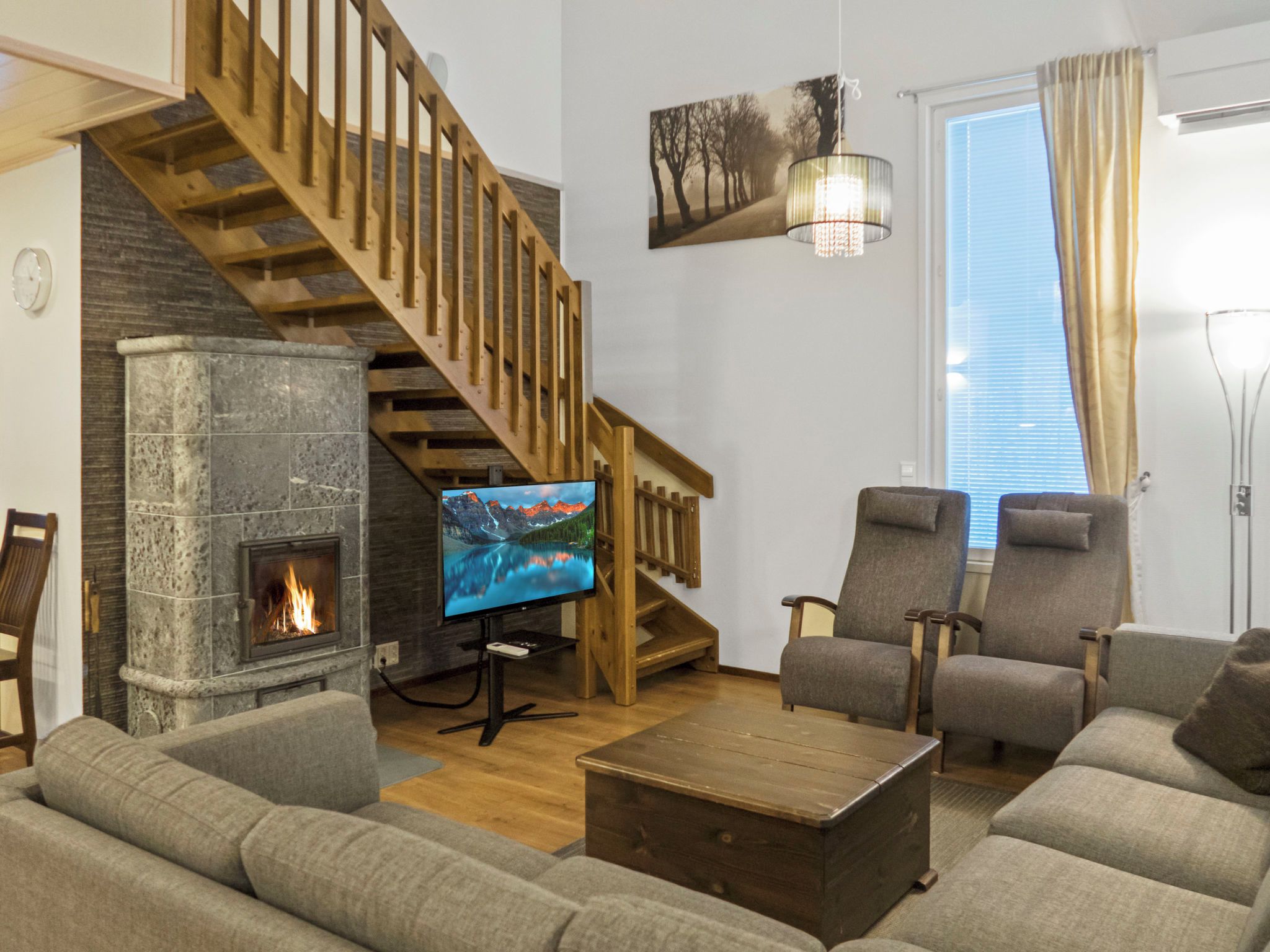 A living room with a stone fireplace, wooden staircase, and a television.