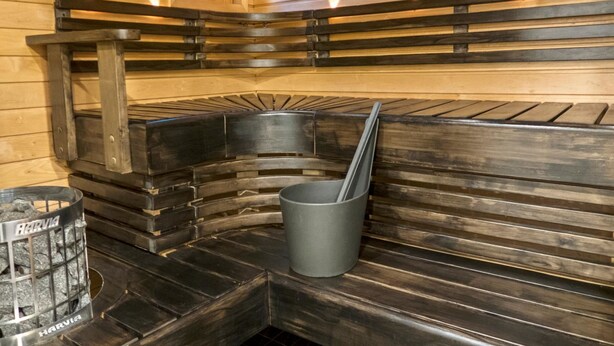 En sauna med træbænke, en metalspand og en Harvia saunaovn.