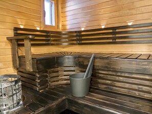 Una sauna con panche in legno, un catino di metallo e una stufa sauna Harvia.