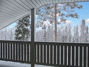 Un espace extérieur abrité, doté d’une rambarde en bois, et entouré d’arbres couverts de neige.