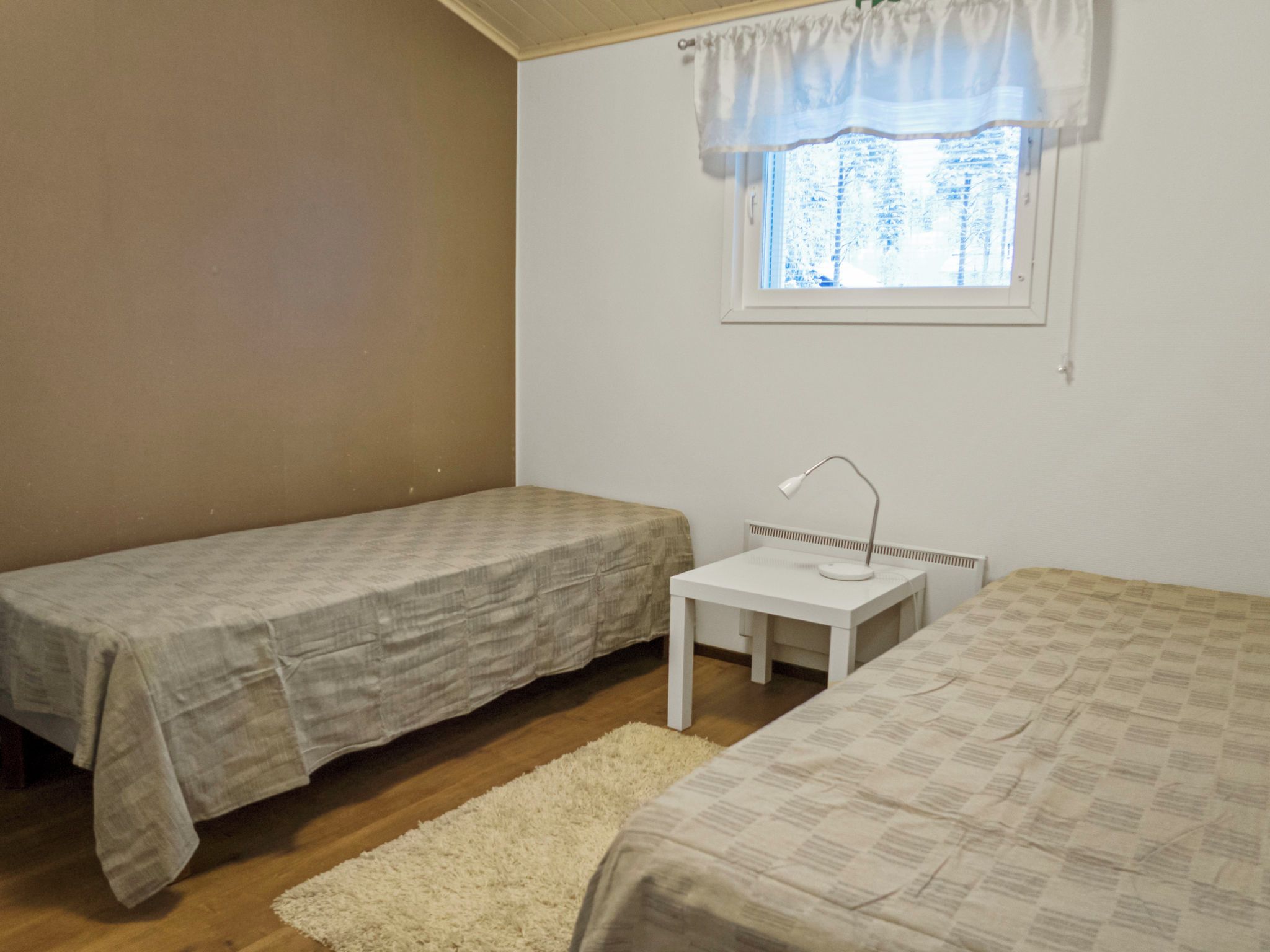 A small, single-bedroom room with two beds, a small table, and a window with a view of trees.