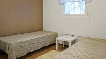 A small, single-bedroom room with two beds, a small table, and a window with a view of trees.