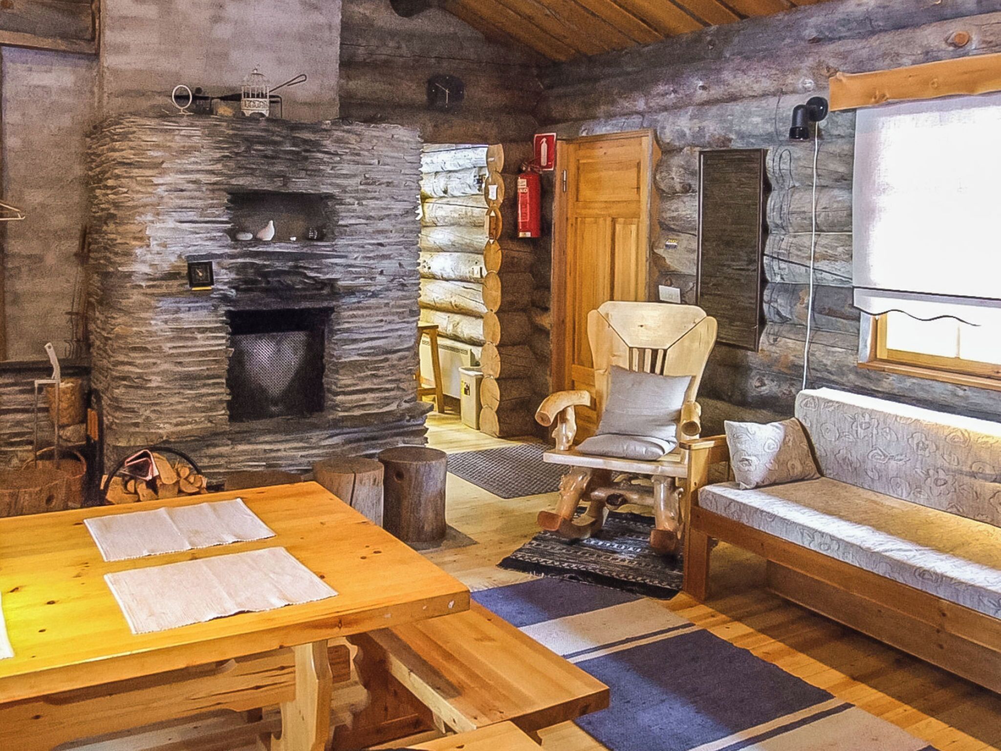 Interior rústico de una cabaña de troncos con chimenea de piedra, muebles de madera y un rincón de estar acogedor.