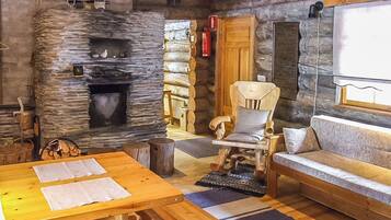 Interior rústico de una cabaña de troncos con chimenea de piedra, muebles de madera y un rincón de estar acogedor.