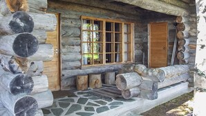 Une cabane en rondins dotée d’un porche pavé de pierres, de portes en bois et d’une fenêtre à carreaux.