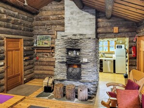 A log cabin interior with a stone fireplace, wooden furniture, and a kitchen area.
