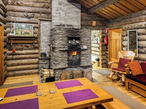 A log cabin interior with a stone fireplace, wooden furniture, and a dining area.