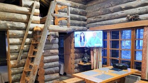 L’intérieur d’une cabane en rondins, avec une échelle en bois, un téléviseur et un coin repas équipé de bancs.