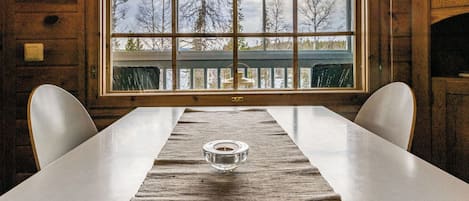 Una habitación con paneles de madera, un gran ventanal, una mesa con sillas y una vela sobre la mesa.
