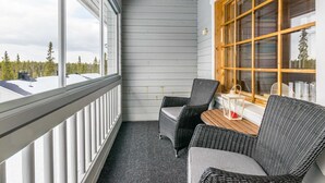 A balcony with two wicker chairs, a small table, and a window with wooden frames.