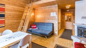 A wooden cabin interior with a sofa, a dining table, chairs, a staircase, and a fireplace.