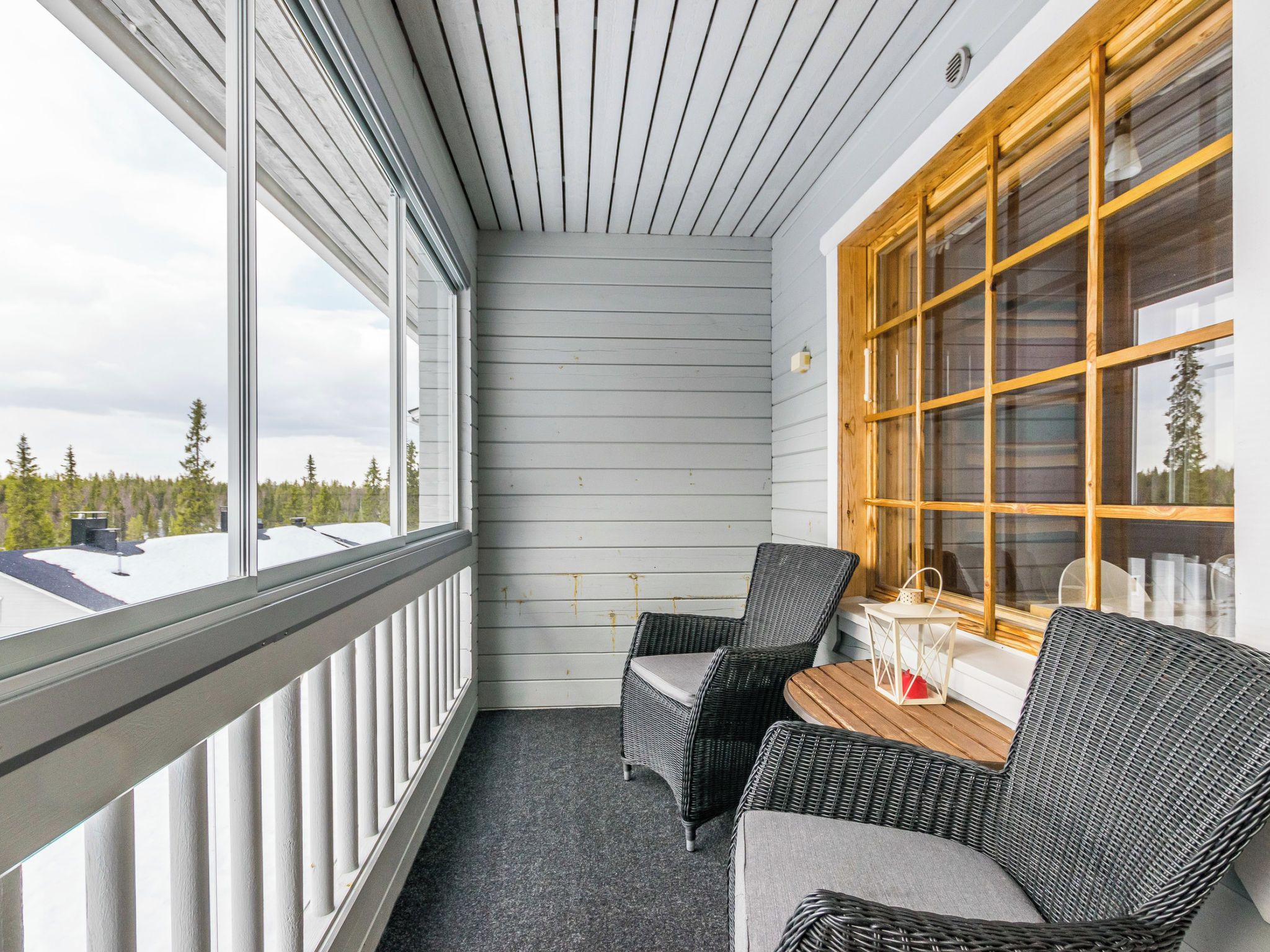 Ein Balkon mit zwei Korbstühlen und einem kleinen Tisch, mit Blick auf eine bewaldete Gegend.