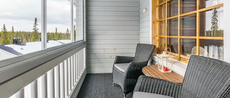 Un balcon avec deux fauteuils en osier et une petite table, donnant sur une zone boisée.