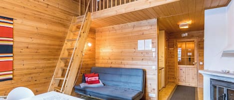 A wooden cabin interior with a sofa, a dining table, and a kitchen area.