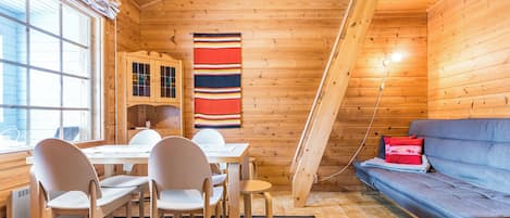 Interior de uma cabana de madeira com área de refeições, um sofá e uma janela.