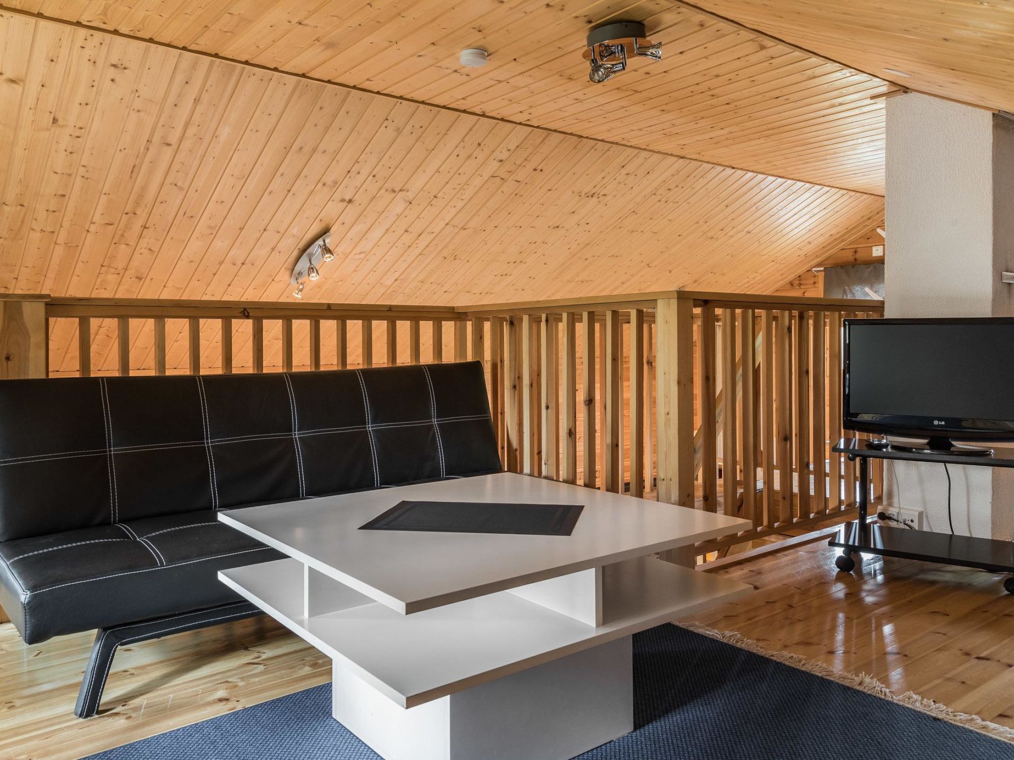 Une pièce chaleureuse avec un canapé noir, une table blanche et un téléviseur posé sur un meuble.
