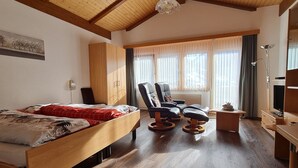 Quarto com cama de madeira, escrivaninha, cadeira e televisão.