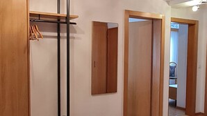Um corredor com piso de madeira, um porta-roupas e um espelho na parede.