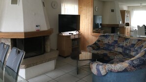 Uma sala de estar com lareira, televisão, sofá e área de jantar.