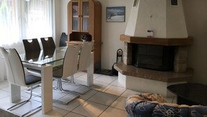 Uma sala de estar moderna com mesa de jantar de vidro, cadeiras, lareira embutida e um espaço de estar aconchegante.