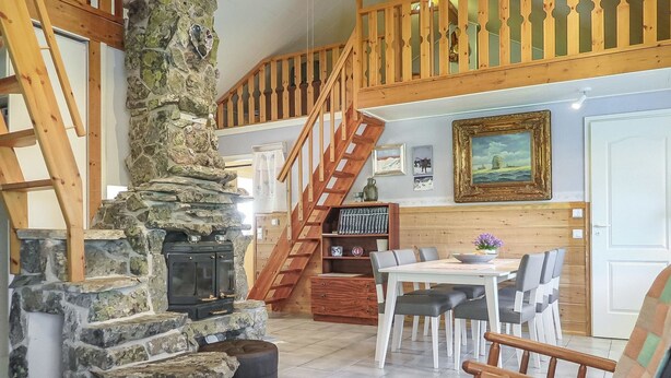 Un intérieur rustique agrémenté d’une cheminée en pierre, d’un escalier en bois et d’un coin repas avec une table et des chaises.