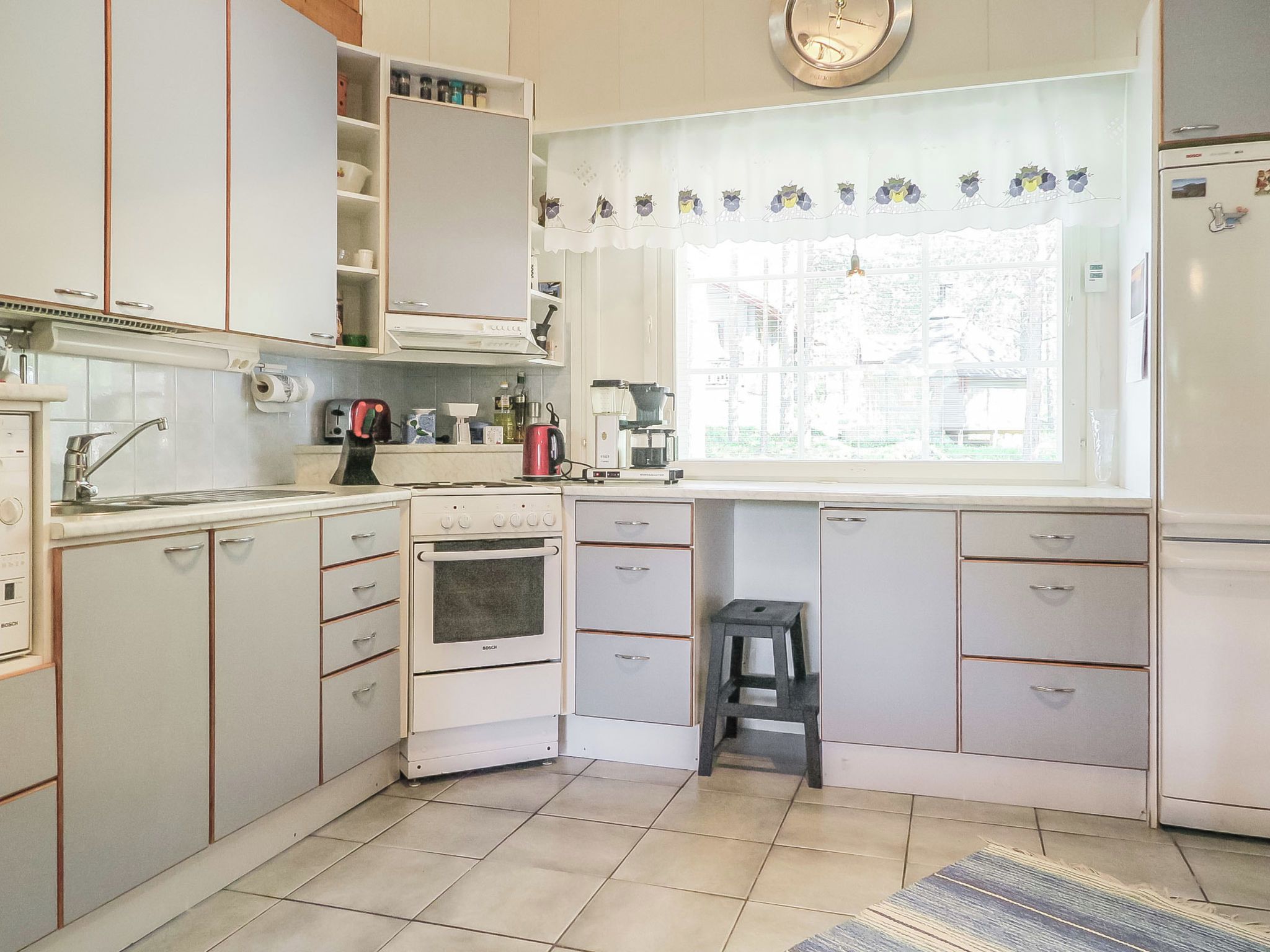 Cucina con mobili bianchi, forno Bosch, macchina da caffè e finestra vista edifici.