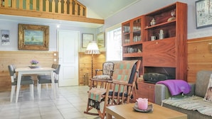 Un salon chaleureux avec une table à manger en bois, un fauteuil à bascule et un canapé. On y trouve une bibliothèque remplie de livres et d’objets décoratifs.