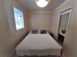 A small, narrow bedroom with a single bed, a window with blinds, a ceiling light, and a mirror on the wall. - Kerkkälä by Interhome (Sodankylä)
