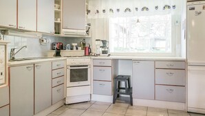 Une cuisine compacte avec des meubles blancs, un four Bosch, un évier et une fenêtre donnant sur l’extérieur.