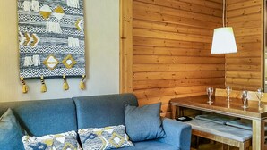 En moderne stue med en blå sofa, et mønstret plaide, træpaneler, et spisebord med stole og en hængende lampe.