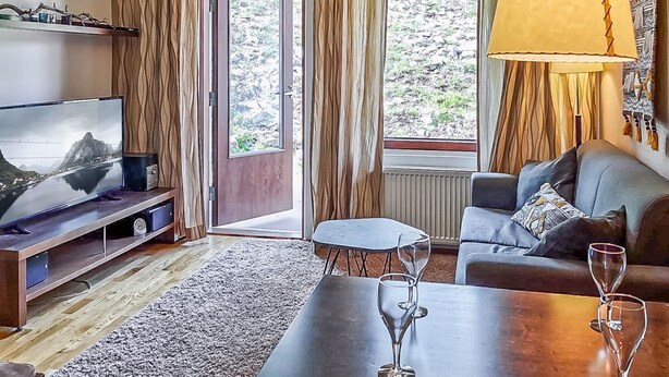 En moderne stue med et fladskærms-tv, en sofa, et sofabord og et spisebord med vinglas.