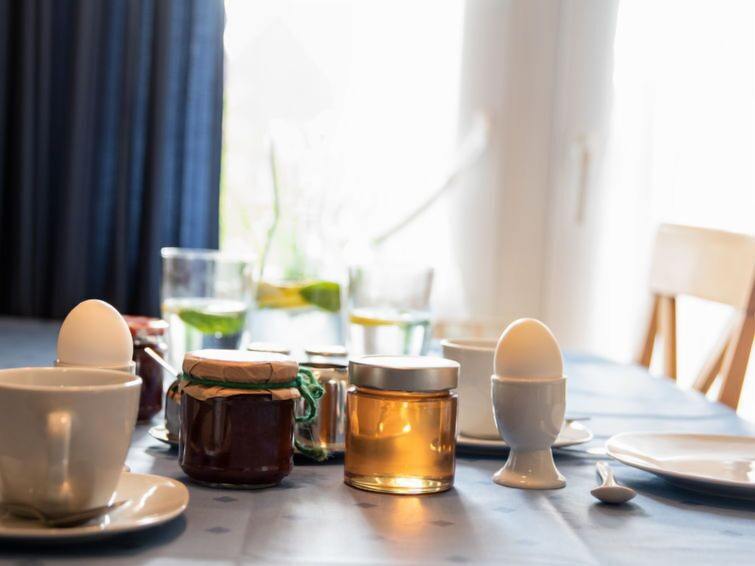 Una mesa de desayuno con huevos, un frasco de mermelada y una vela.