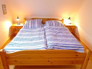 Uma cama de madeira com roupa de cama listrada, duas luminárias de cabeceira e uma mesinha de apoio em cada lado.