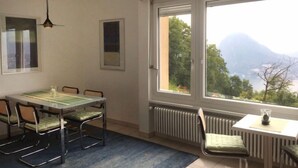 Een kamer met een eettafel, stoelen, een radiator en een groot raam met uitzicht op de bergen.