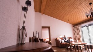 A cozy living room with a wooden ceiling, a sofa, a coffee table, and a dining table. - Monte Rosa by Interhome (Saas-Grund)