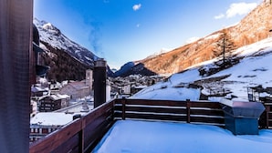 A snow-covered balcony with a wooden railing overlooking a mountainous landscape and a town below. - Monte Rosa by Interhome (Saas-Grund)