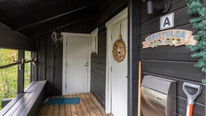 Eine Holzveranda mit einer Bank, einer Tür, einem Kranz und einem Schild mit der Aufschrift 'TERETULOA'.