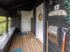 Un porche de madera con un banco, una puerta, una guirnalda y un letrero que dice 'TERVETULOA'.