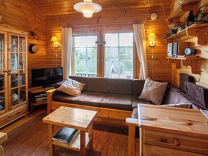 Interior acogedor de una cabaña con piso de madera, un sofá, un televisor y una mesa de comedor.