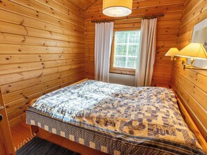 Una habitación de madera con una cama, una ventana con cortinas y una lámpara.