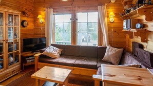Ein gemütliches Blockhausszimmer mit Holzvertäfelung, einer Sitzecke, einem Fernseher und einem Esstisch.