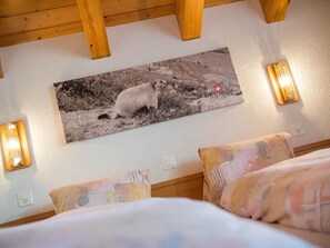 A bedroom with a bed, two wall-mounted lamps, and a painting of a sheep on a mountain. - Helvetia Apartments by Interhome (Saas-Fee)